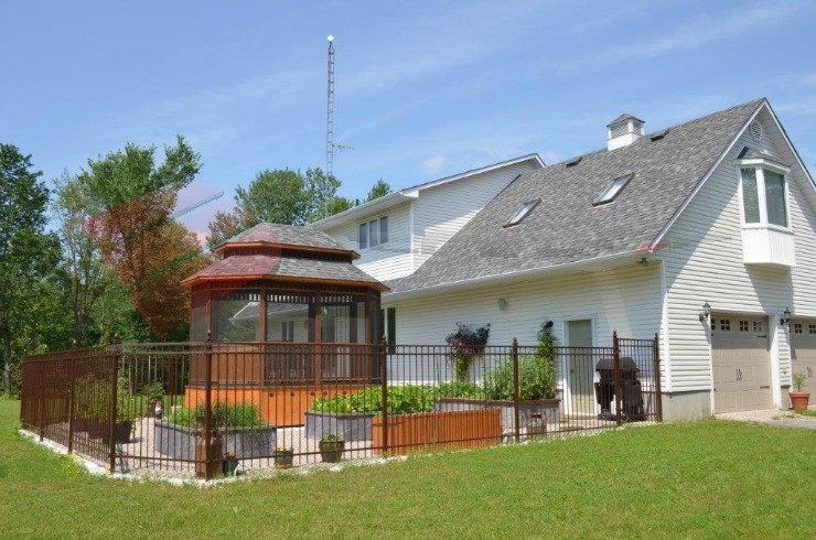 Enclosed gazebo enhanced with a warm stain, situated in a side-yard gated with an iron fence